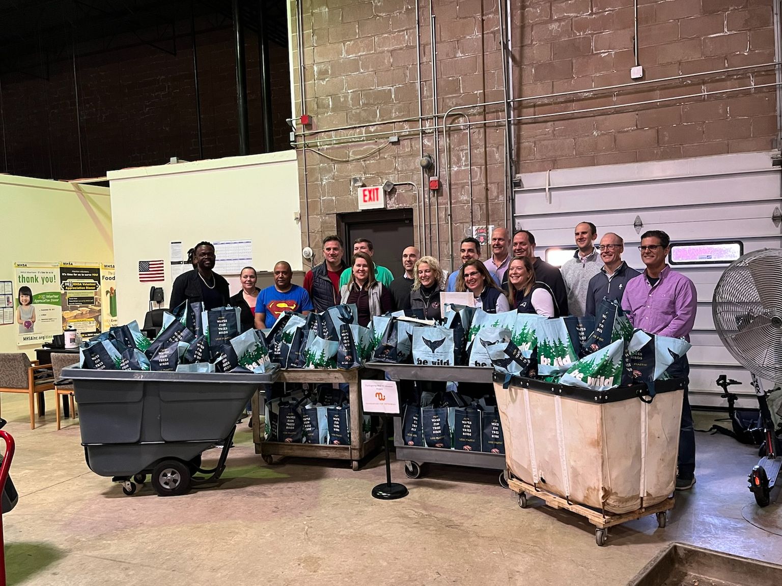 Group of people smiling for photo in a warehouse, posing with carts full of reusable bags.