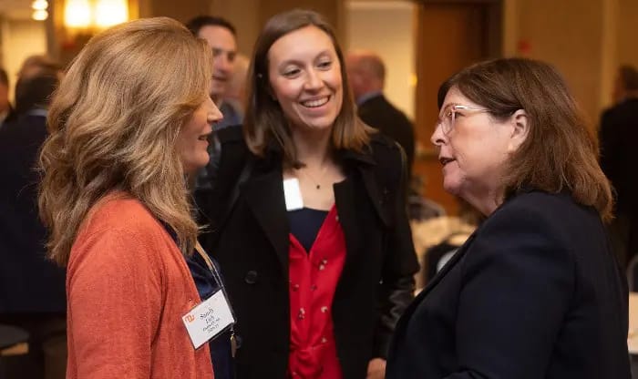 Three women in business attire with name tags in a conversation.