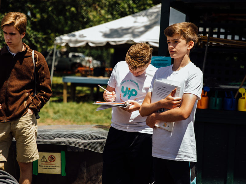 Teenagers standing outside in front of tent, holding papers.