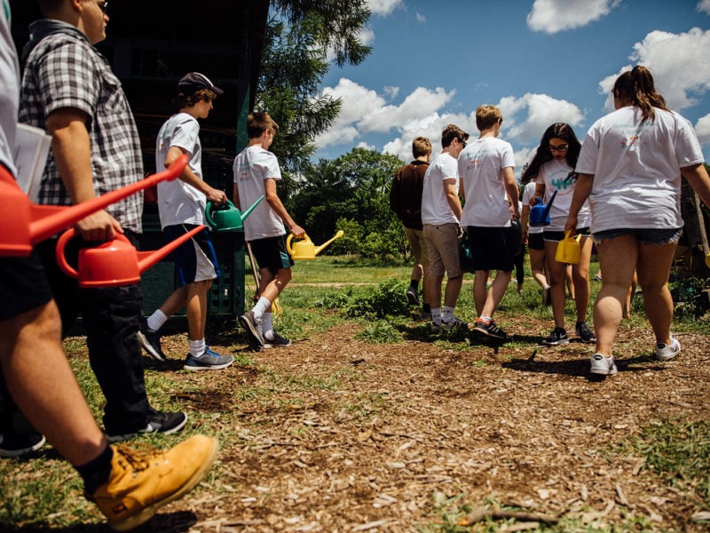 Image of group of teenagers outside walking with watering cans.