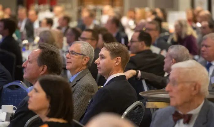 Crowd of people seated in business attire, looking in the same direction.