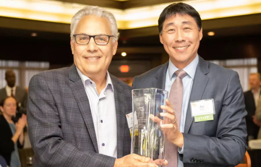 2 people pose for photo in suits with glass award.
