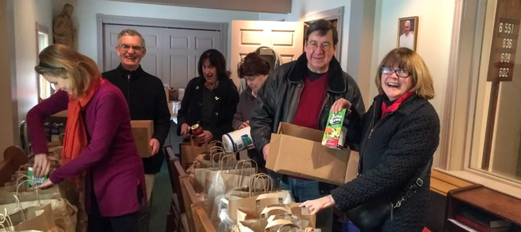 Group of people inside smiling, packing food into paper bags.