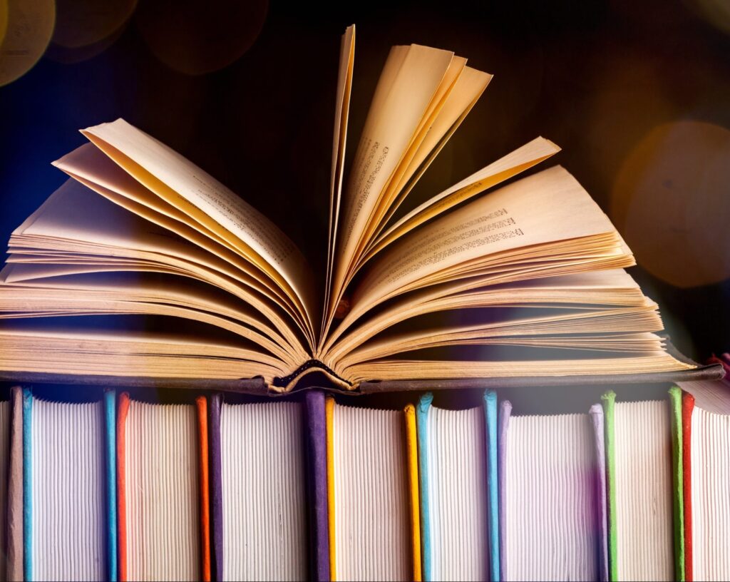 Book open with pages fanned out, resting on top of other books.