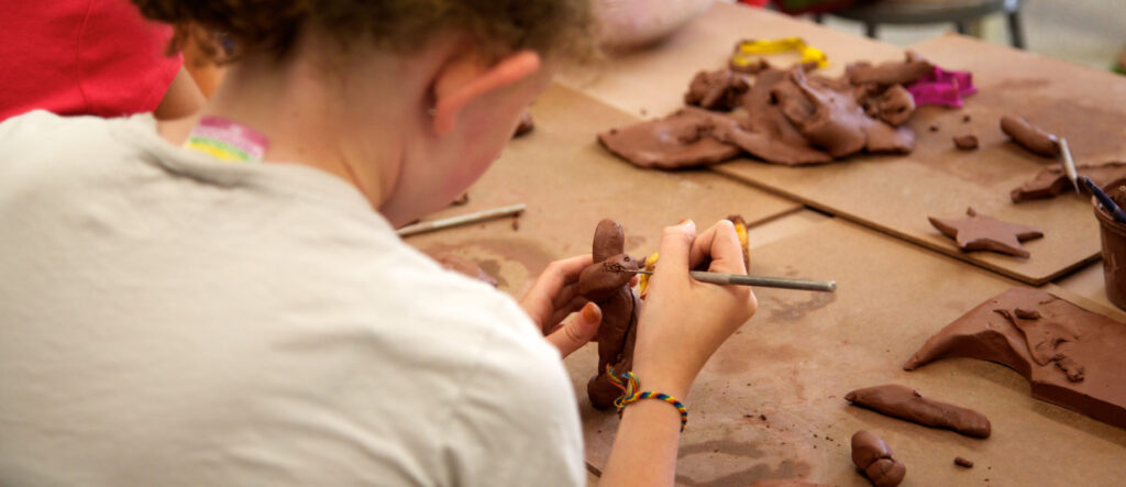 Image of back of young person carving red clay with metal tool.